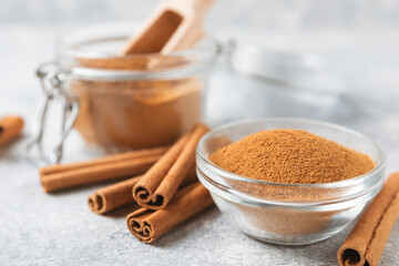 Cinnamon powder in a bowl on a textured wooden background. Spicy spice for baking, desserts and drinks. Fragrant ground cinnamon. Cinnamon stick. Place for text. Copy space.