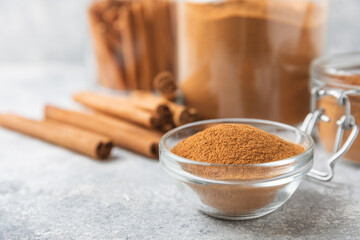 Cinnamon powder in a bowl on a textured wooden background. Spicy spice for baking, desserts and drinks. Fragrant ground cinnamon. Cinnamon stick. Place for text. Copy space.
