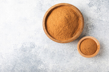 Cinnamon powder in a bowl on a textured wooden background. Spicy spice for baking, desserts and drinks. Fragrant ground cinnamon. Cinnamon stick. Place for text. Copy space.