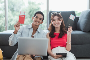 A couple is sitting on the floor with a laptop and tablet in front of them, holding passport and reservation hotel and ticket for journey together