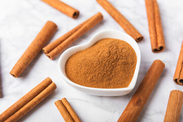 Cinnamon powder in a bowl on a textured wooden background. Spicy spice for baking, desserts and drinks. Fragrant ground cinnamon. Cinnamon stick. Place for text. Copy space.