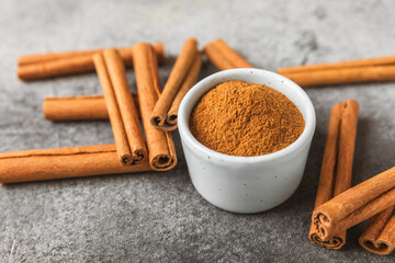 Cinnamon powder in a bowl on a textured wooden background. Spicy spice for baking, desserts and drinks. Fragrant ground cinnamon. Cinnamon stick. Place for text. Copy space.