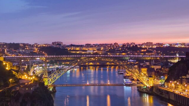 Day to night transition aerial close up view of the historic city of Porto, Portugal timelapse with the Dom Luiz bridge. Illuminated waterfront and curved river from above