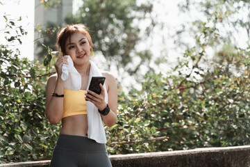 A woman is standing outside with a towel and a cell phone.She is jogging in the morning for good health and slim fit.