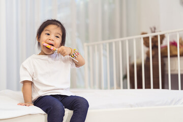 A young girl is sitting on a bed with a lollipop in her mouth