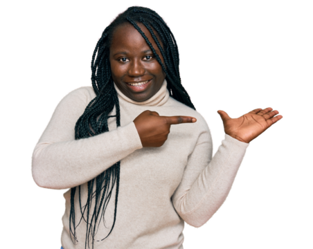 Young black woman with braids wearing casual winter sweater amazed and smiling to the camera while presenting with hand and pointing with finger.