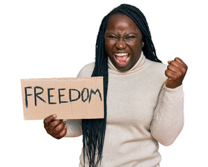 Young black woman with braids holding freedom banner screaming proud, celebrating victory and...