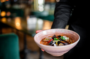 A close-up view of a person serving a bowl of delicious seafood soup, capturing the essence of fine dining. The vibrant colors and textures make it visually appealing