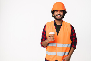 Happy young Indian construction worker in orange uniform and helmet drinking coffee isolated over...