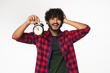 Panicking young Indian man holding clock hurrying up isolated over white background. Hindi boy...