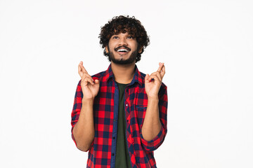 Happy young Indian man in casual clothes making wish with fingers crossed isolated over white background. Hindi boy praying, expecting good changes, asking God - obrazy, fototapety, plakaty