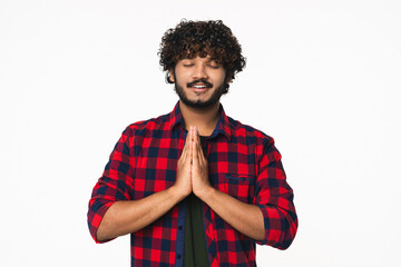 Young Indian man praying to God with closed eyes isolated over white background. Hindi cheerful boy...