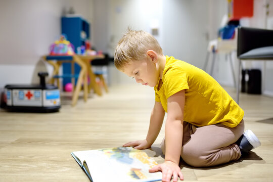 Cute little boy reading a book on the floor in a kindergarten. The child has time in the preschool
