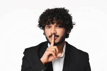Attractive young Hindu businessman with finger on lips isolated over white background. Handsome Indian manager CEO boss having secret , showing silent gesture - obrazy, fototapety, plakaty