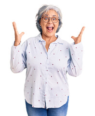 Senior woman with gray hair wearing casual business clothes and glasses celebrating victory with happy smile and winner expression with raised hands