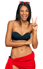 Fototapeta premium Young african american woman wearing bikini smiling with happy face winking at the camera doing victory sign. number two.
