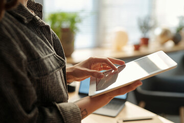 Hand of unrecognizable businesswoman in grey casualwear keeping fingertips on screen of tablet...