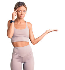 Beautiful caucasian woman wearing sportswear confused and annoyed with open palm showing copy space and pointing finger to forehead. think about it.