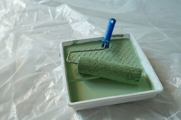 Paintroller with blue plastic handle and green paint in square tray standing on the floor covered with cellophane during renovation work - 775060828