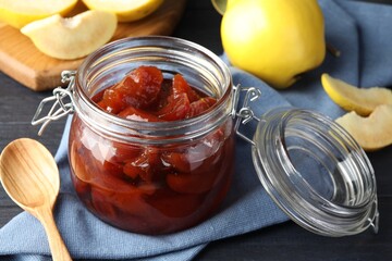 Quince jam in glass jar, spoon and fresh raw fruits on grey table, closeup