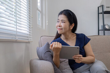Elderly woman's leisure day watching social media on tablet, watching news on sofa in living room