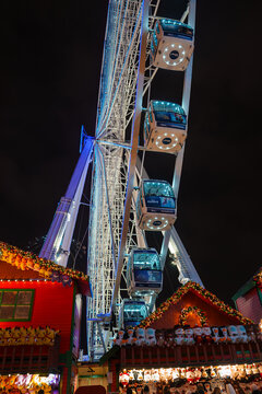 Illuminated Ferris wheel towers over traditional Europeanstyle Christmas market Winter Wonderland stalls adorned with festive lights in London, UK, creating a magical holiday atmosphere at night.