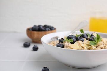 Tasty oatmeal with blueberries, mint and almond flakes in bowl on white tiled table, closeup. Space for text