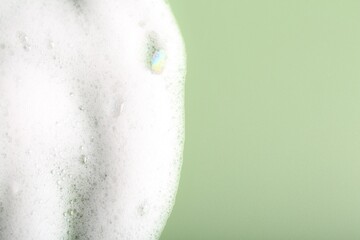 White fluffy foam on green background, top view. Space for text