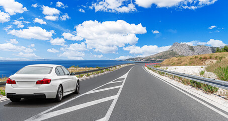 A white car drives along the sea coastline on a sunny summer day.