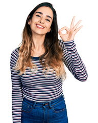 Beautiful hispanic woman wearing casual striped shirt smiling positive doing ok sign with hand and fingers. successful expression.