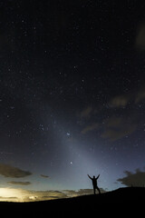 A stargazer having his hands open wide in the night sky silhuette showing the zodiacal light in the sky.