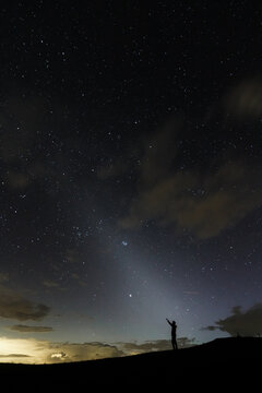A stargazer poining up in the night sky silhuette showing the zodiacal light in the sky.