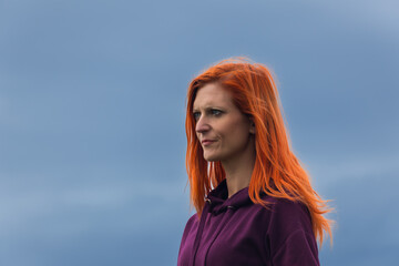 Portrait of redheaded pensive young woman against blue cloud