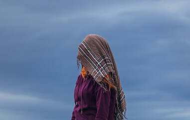 Portrait of young woman covered head with scarf against blue cloud. Faceless concept - 775077215