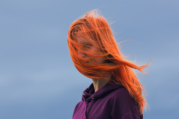 Portrait of redheaded young woman with blowing hair against blue cloud