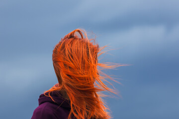 Portrait of redheaded young woman with blowing hair against blue cloud