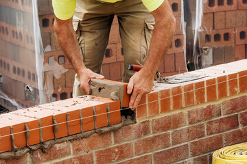 Industrial bricklayer laying bricks on cement mix on construction site