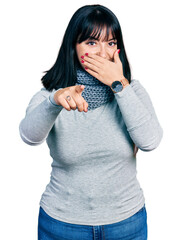 Young hispanic plus size woman wearing winter scarf laughing at you, pointing finger to the camera with hand over mouth, shame expression