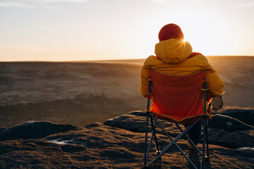 A woman in an yellow jacket relaxing alone on the top of mountain  at sunrise or sunset on spring cold day. Travel  Lifestyle concept