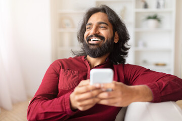Man laughing holding smartphone, relaxing at home