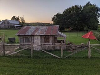 A chicken coop on a lawn behind a fence at sunset © Matt