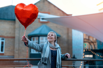 middle-aged happy woman with a heart-shaped balloon falling a love, having a fun day, walking...