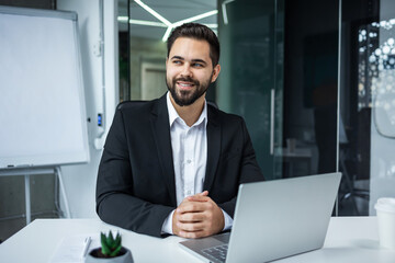 portrait of a happy bearded handsome man at workplace at computer desk in office. Business male employee entrepreneur or manager sitting at work look pensive
