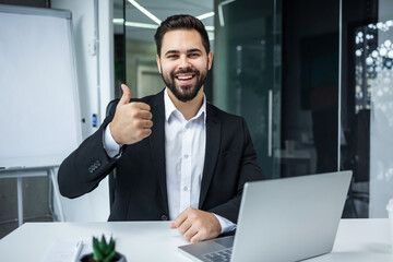 Portrait of handsome bearded man in formal suit smiling and showing thumb up gesture in modern office - 775083654
