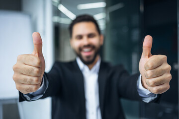Positive young man showing thumb up sign over office background. Winner. Success. Body language. office background - 775083663