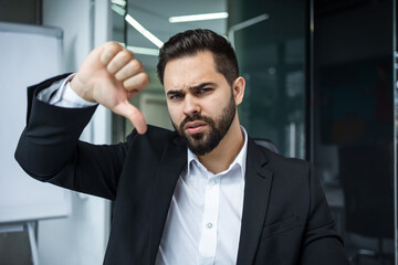 Portrait of Unhappy man Showing Thumb Down Sign sit at work desk at the office. Gesturing Dislike and Disagreement Sign by using a finger sign. - 775083690