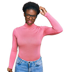 Fototapeta premium Young african american girl wearing casual clothes and glasses confuse and wonder about question. uncertain with doubt, thinking with hand on head. pensive concept.