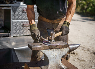 The farrier hammers the hot horseshoe on the anvil with a hammer on the farm in a sunny day. Horseshoeing.