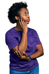 African american woman with afro hair wearing casual purple t shirt with hand on chin thinking about question, pensive expression. smiling with thoughtful face. doubt concept.