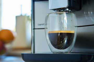 Fresh espresso in clear glass at morning. Coffee machine in kitchen, close up. Modern coffee maker...